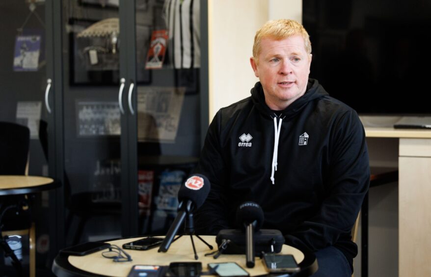 Neil Lennon sits at a table in front of the media's microphones.