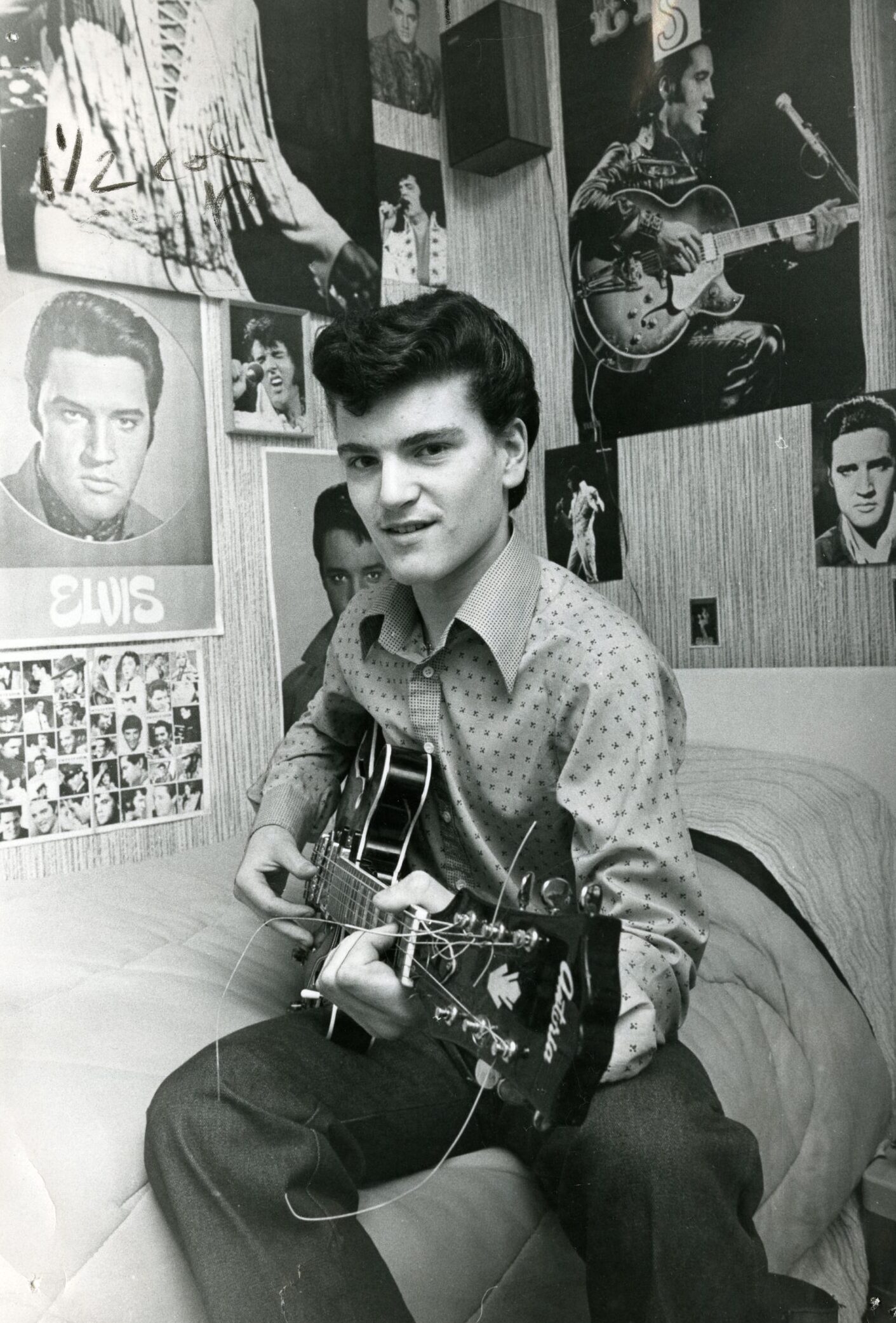 Pupil Derek Parkin holds his guitar on his bed, surrounded by Elvis posters