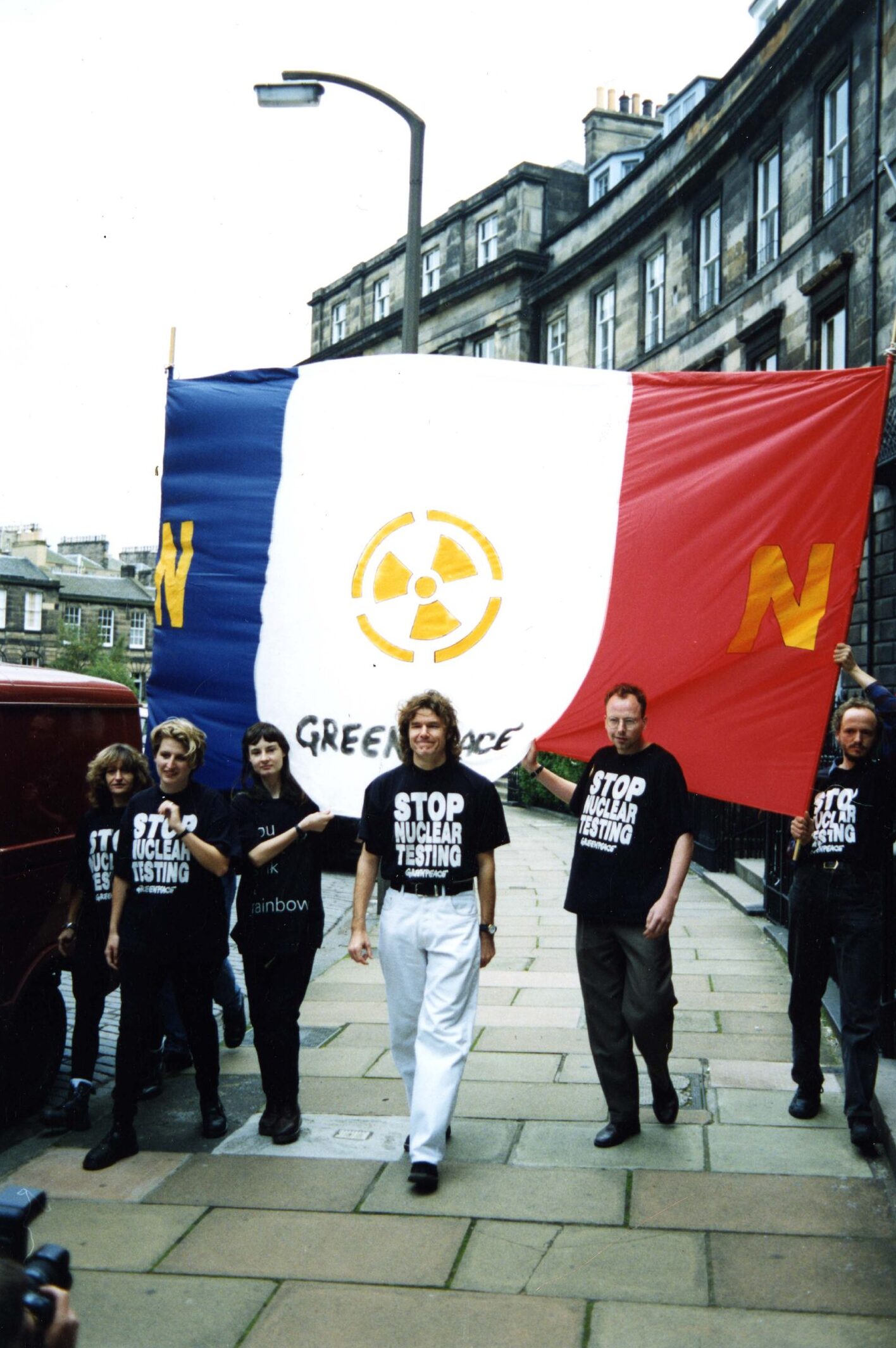 Stuart Adamson and fellow protesters with a large France flag bearing the CND logo on an Edinburgh street as he leads the march against French nuclear tests.