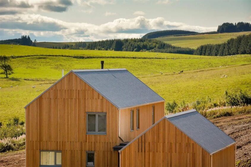 One of the houses in the foreground with gently rolling hills and woodland in the background. 