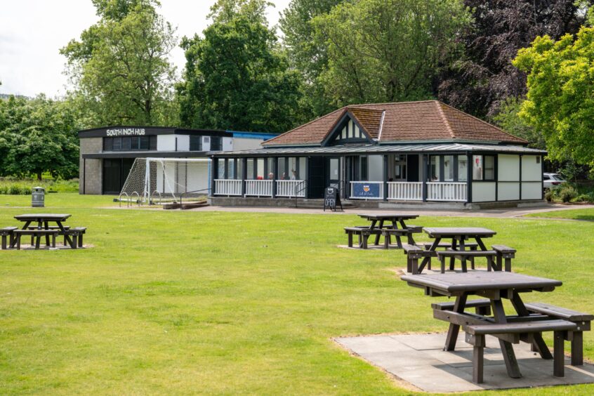 South Inch pavilion exterior with wooden tables and chairs and large expanse of grass