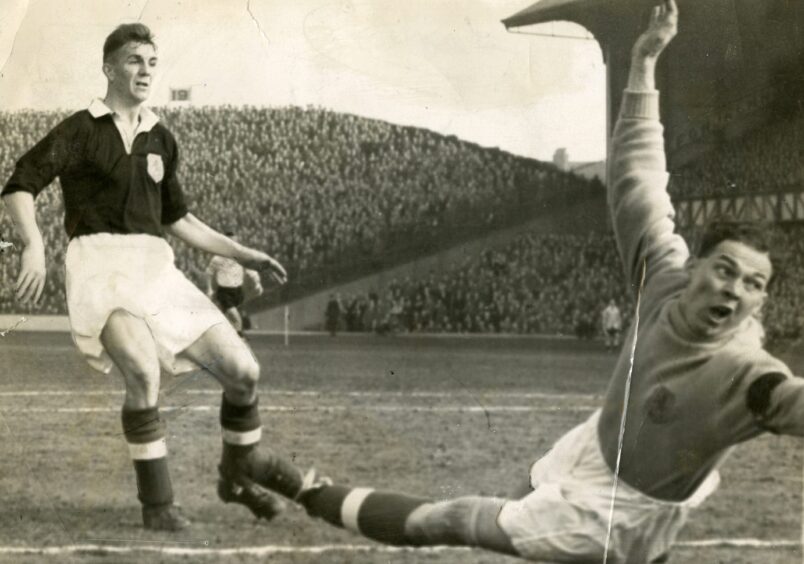 packed stands in the background as the goalie dives for the ball and Doug Cowie looks on