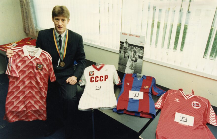Baltacha, wearing a suit, sits on a table beside some of his football memorabilia in 1992.