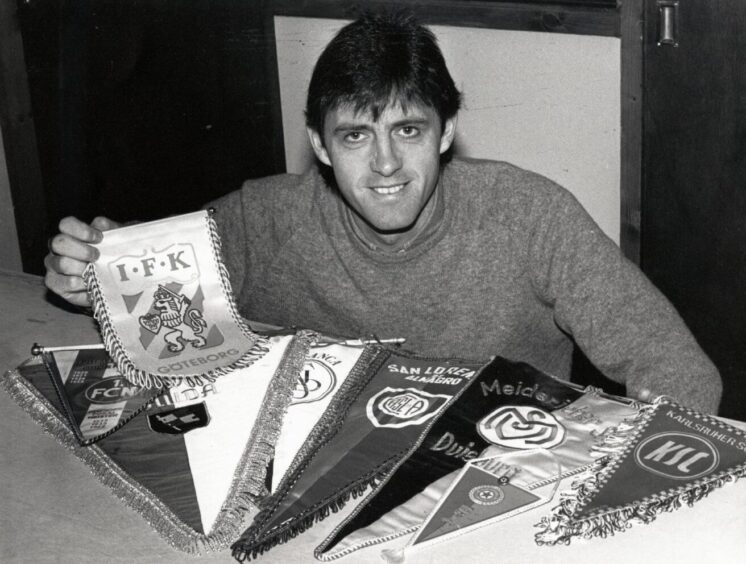 David Narey kneels beside a table bearing some pennants from the teams Dundee United played in European competition