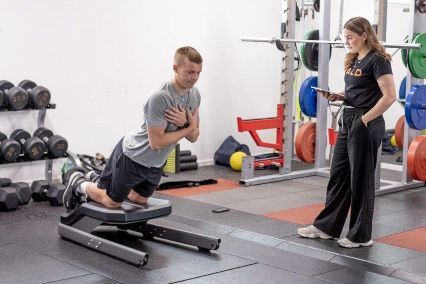 Ewan McLeod leans forwards with his arms folded on his chest as he undergoes a hamstring test.