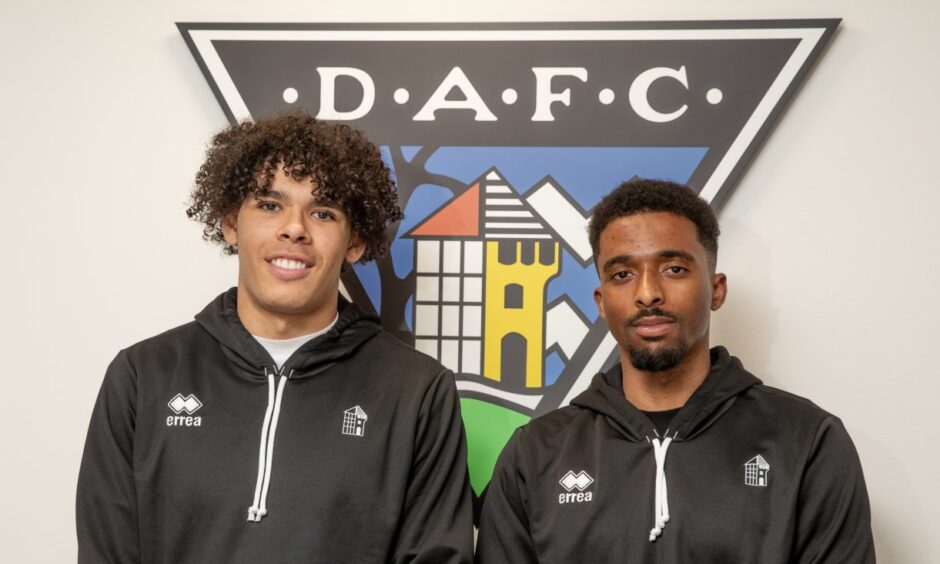 Jeremiah Chilokoa-Mullen and Tashan Oakley-Boothe stand in front of a large DAFC badge on the wall.