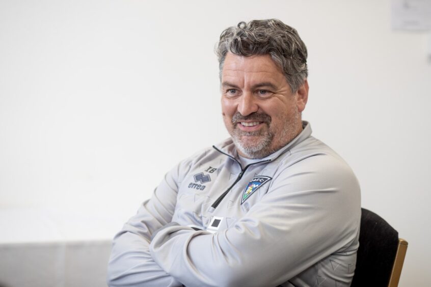 A smiling Iain Brunskill sits with his arms folded.