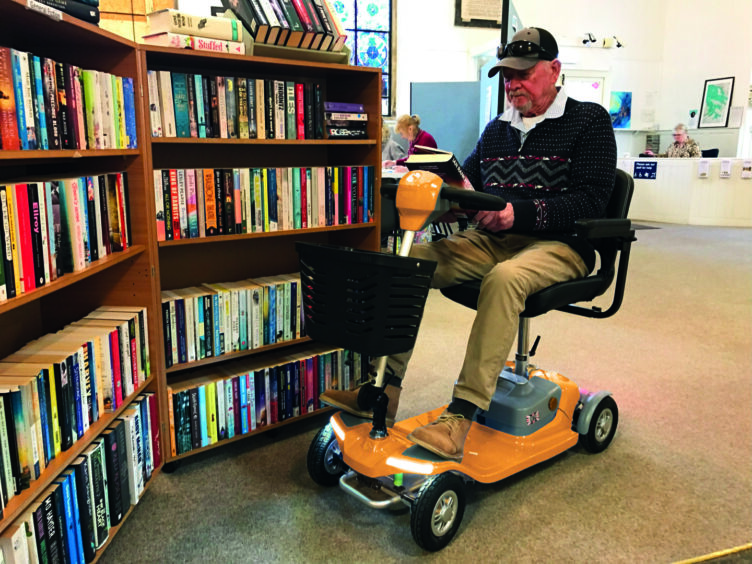 man on a scooter looks at a book in a library