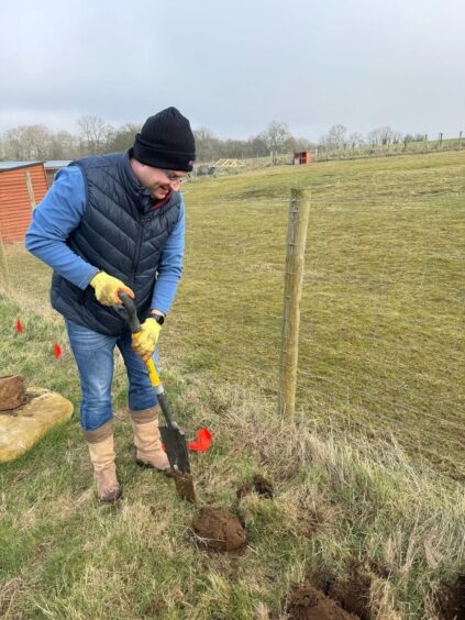 man from Proctor Group uses a shovel to dig up earth in a field