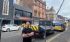 Craig Fraser, arms folded with That Bar and burnt out building behind him