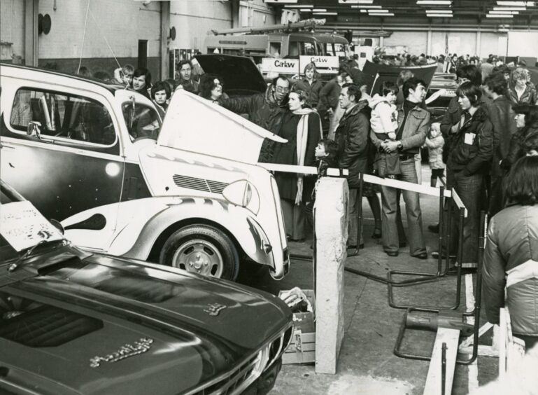 people gather around a car with its bonnet up
