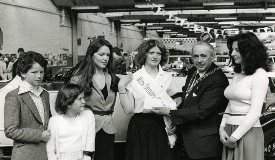 two children and two women look on as Miss Dundee Motor Show is presented with a sash by the Lord Provost.