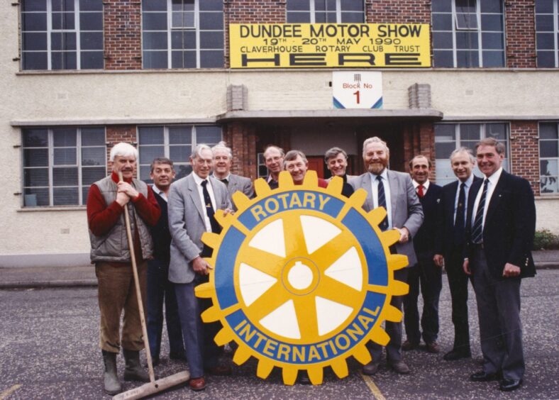 Rotary Club members hold up a big rotary international sign outside the building hosting the 1990 Dundee Motor Show