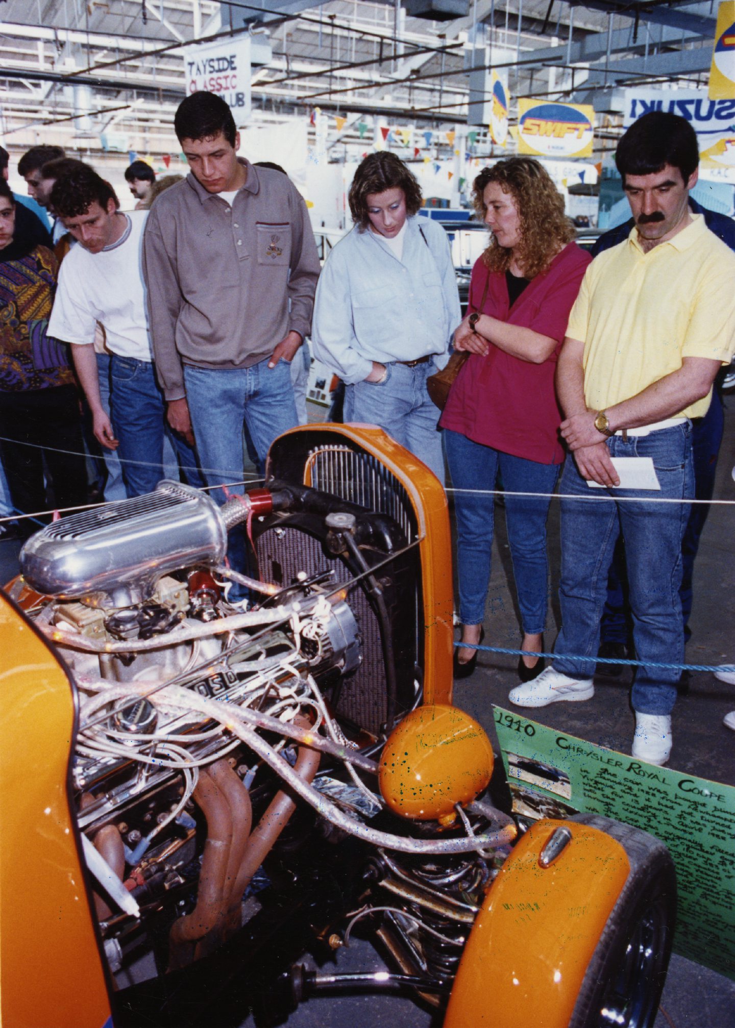 people look at the exposed engine of a custom car