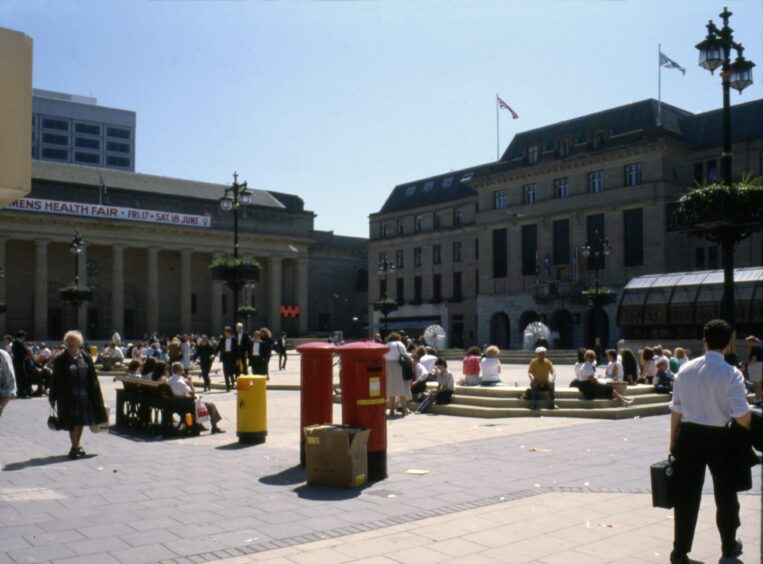 Dundee City Square is busy with people walking and sitting down on a sunny day
