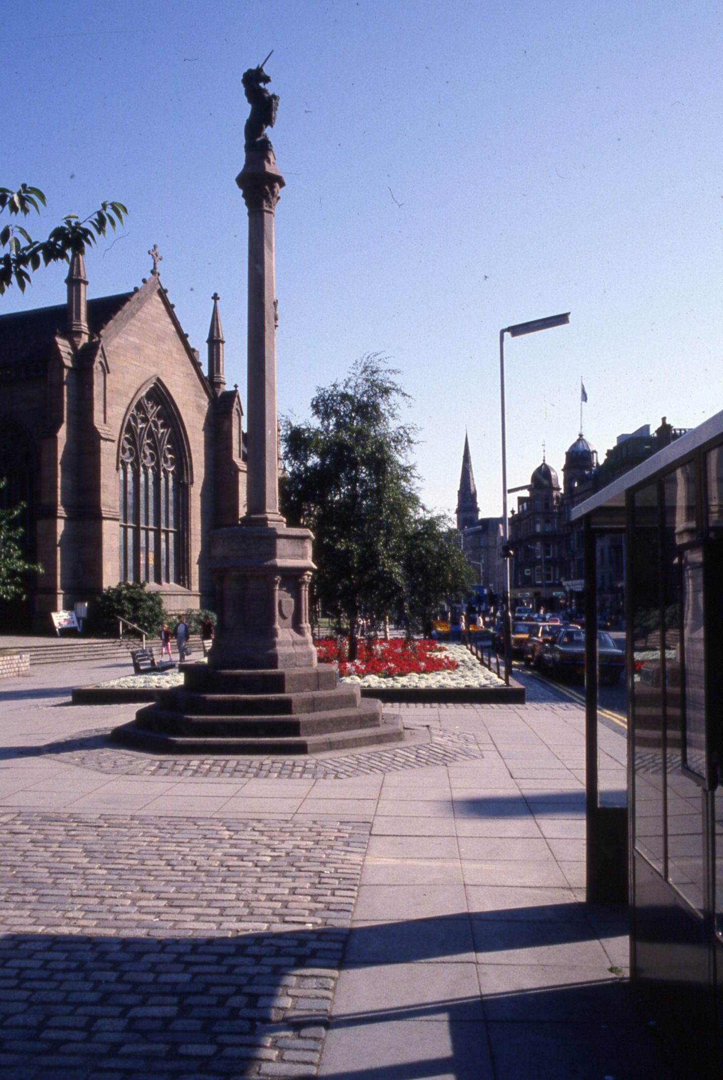 a bus stop next to a church and a market cross with a unicorn at the top