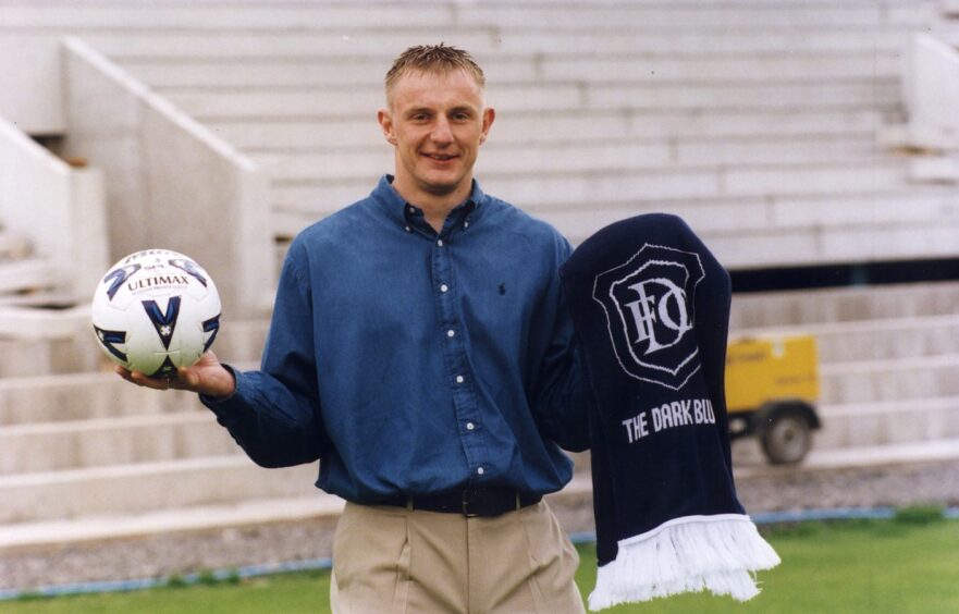Robert Douglas holds a football and a Dundee FC scarf while standing on the Dens Park pitch