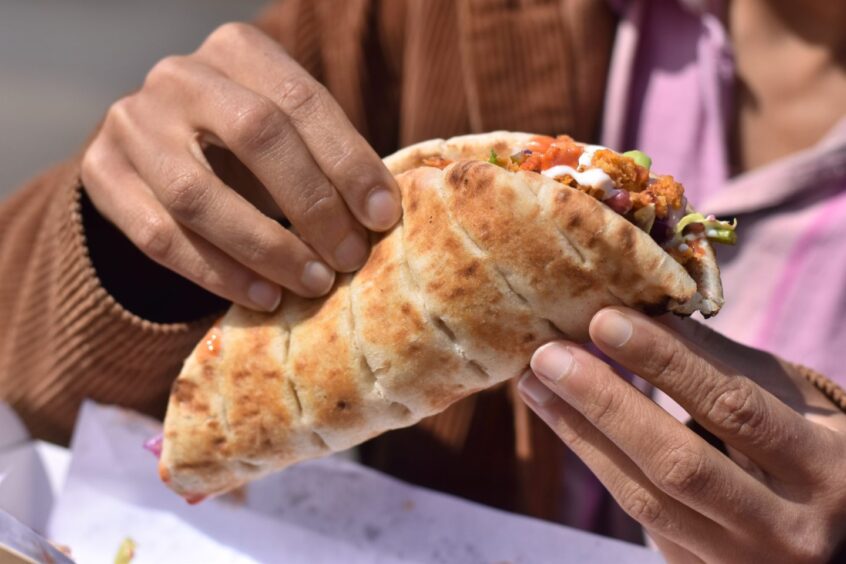 A close-up image of a woman holding a shawarma