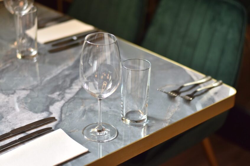 A set table in a restaurant, complete with cutlery and wine glass.