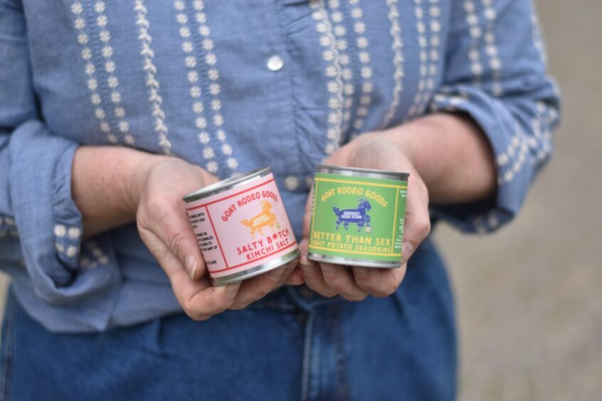 A woman holding two small tins filled with spice blends from Goat Rodeo Goods.