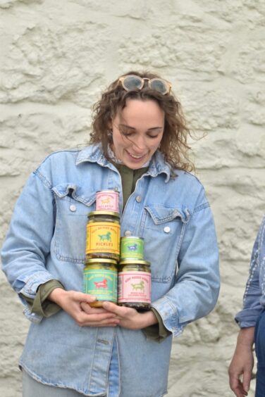 A woman holding multiple jars of Goat Rodeo Goods pickles and spices.