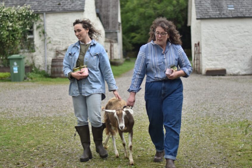 Lucy Patto Davidson and Kat Goldin walking a goat through a farmyard.