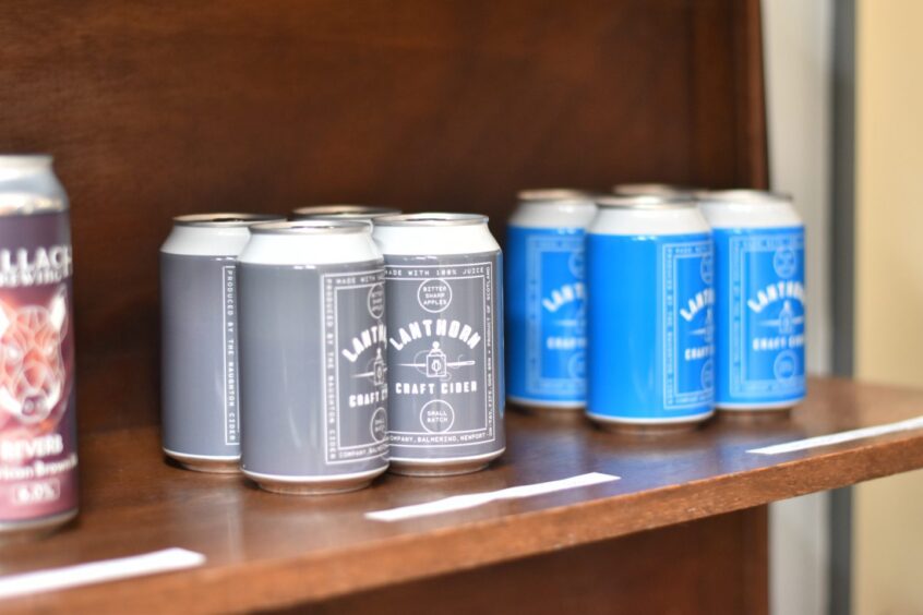 Cans of beer for sale, sitting on a wooden shelf.