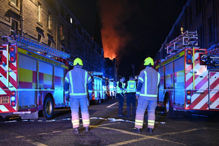 Firefighters lit by blue lights watching building ablaze
