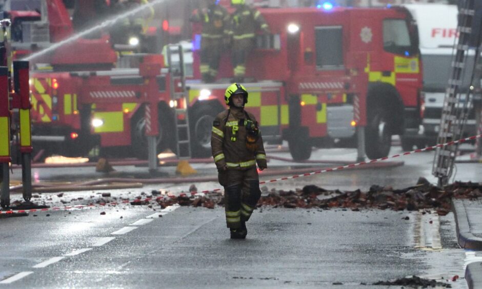 Firefighter with rubble across street and a number of fire engines behind him