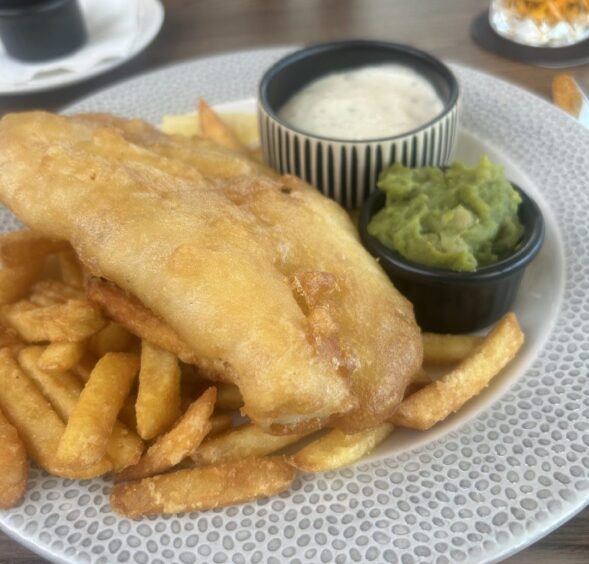 A plate of fish and chips with tartare sauce and mushy peas.
