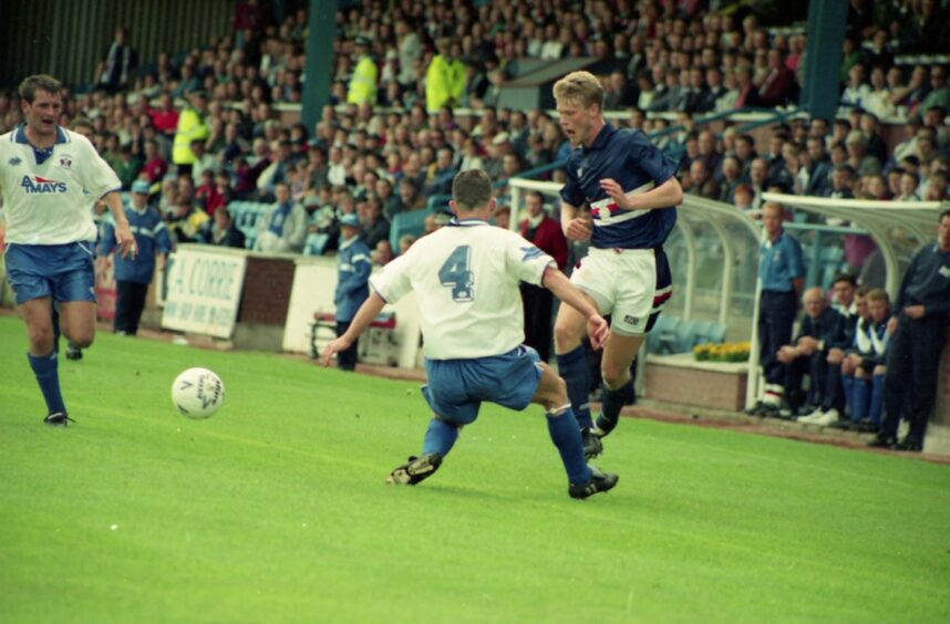 Wieghorst in action against Kilmarnock, playing the ball between two defenders while the crowd looks on