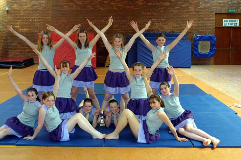 The girls in their outfits celebrating with the trophy in a gym hall in 2001.