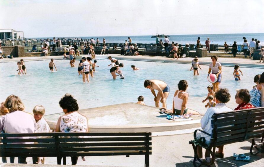 People in the West Links paddling pool and on benches by its side.