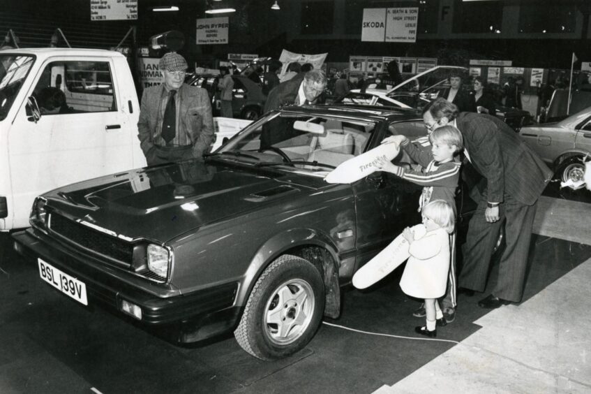 a man and two kids look inside a car 