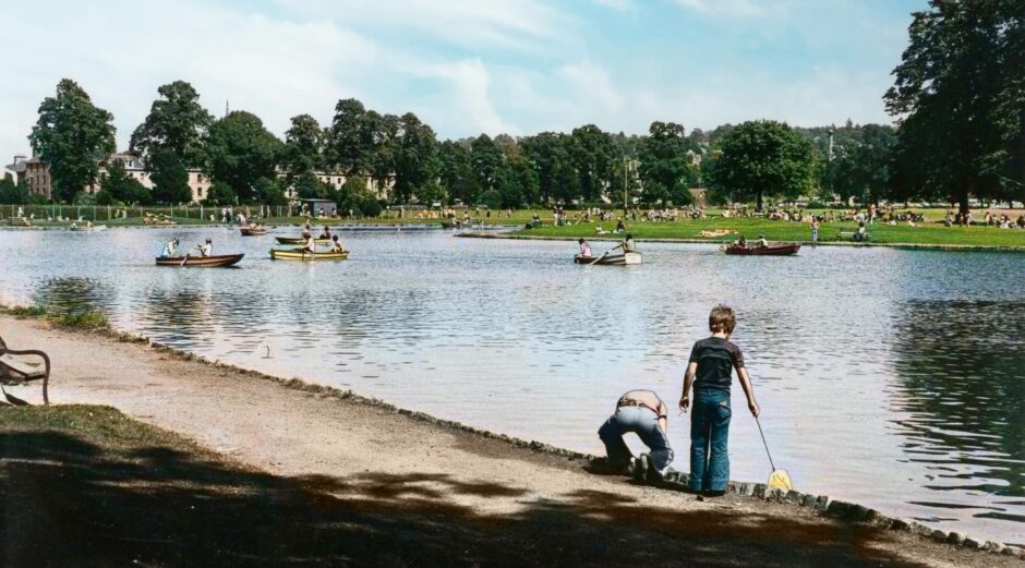 A child is fishing at the boating pond in 1977, while others row boats.