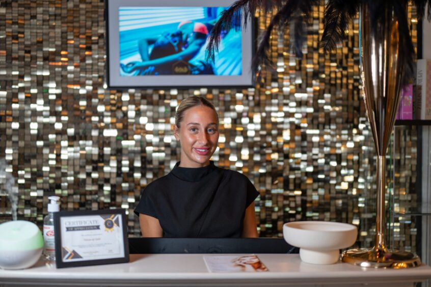 A smiling woman standing behind the desk of a beauty parlour.