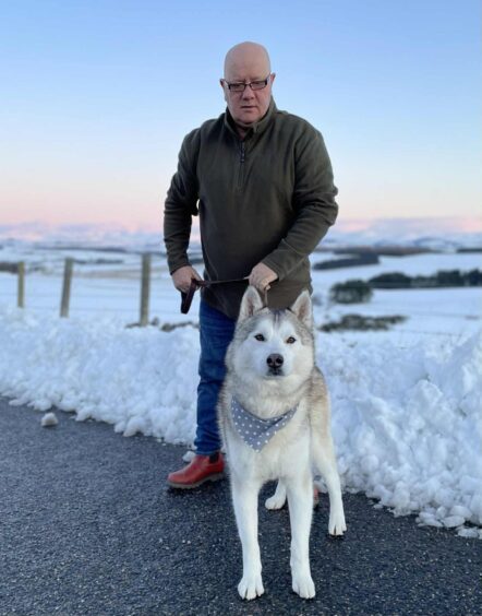 Colin holding a dog on a leash with snow behind them. 