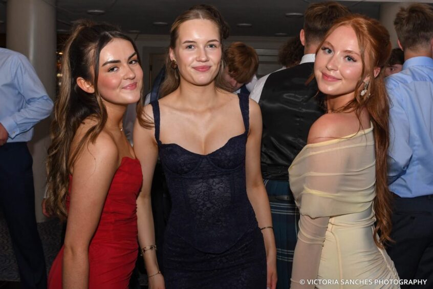 Three girls smiling at a school leavers' prom. 