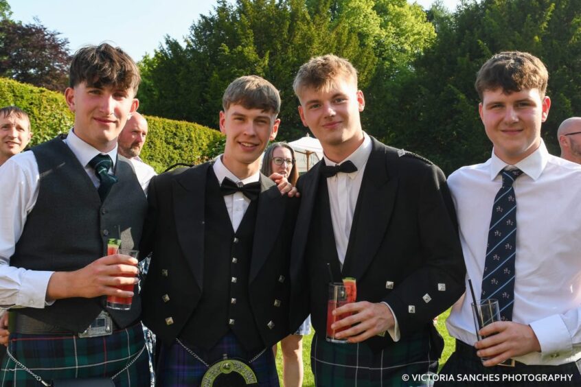 Four boys standing outside with a drink. 