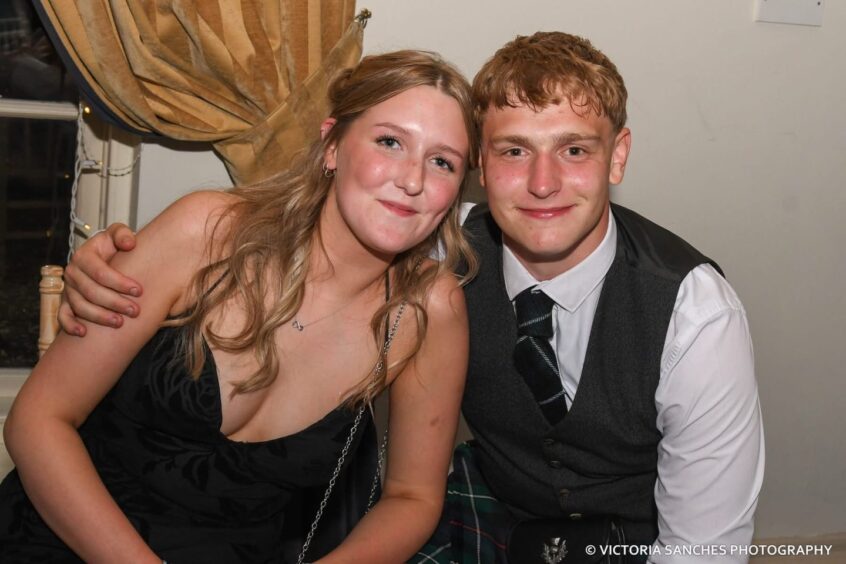 A boy with his arm around a girl, posing for a photo. 