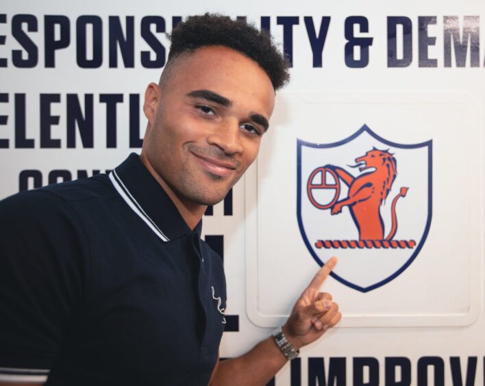 Jai Rowe points to a Raith Rovers crest on the wall.