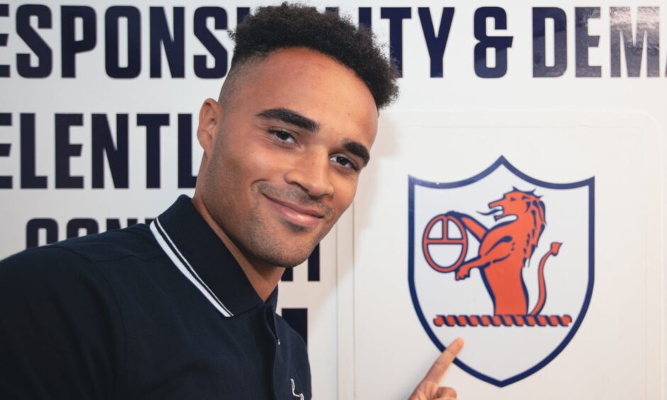 New signing Jai Rowe points to a Raith Rovers badge on the wall.