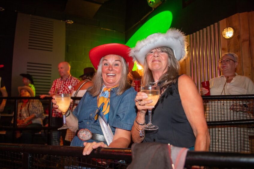 Two women in cowboy hats each with a glass of white wine in a nightclub. 