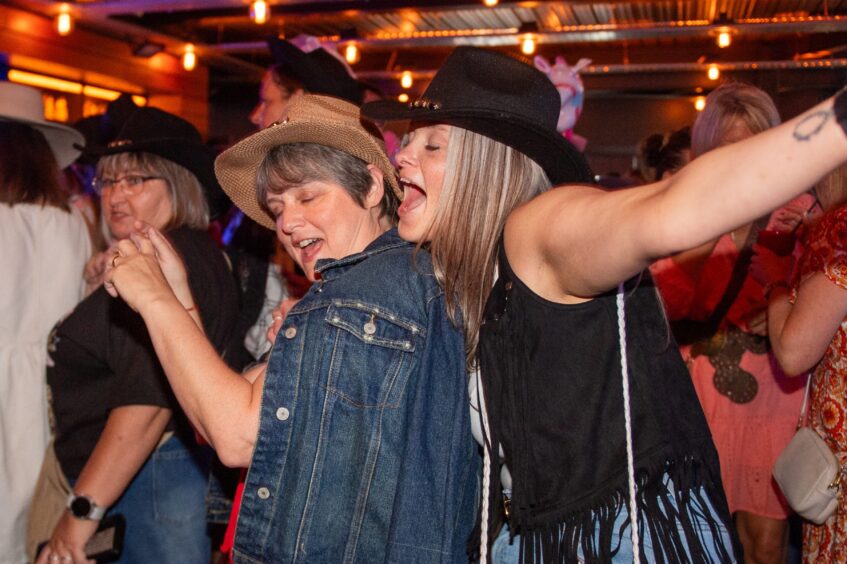 Two women in cowboy hats sing along to music in a nightclub. 
