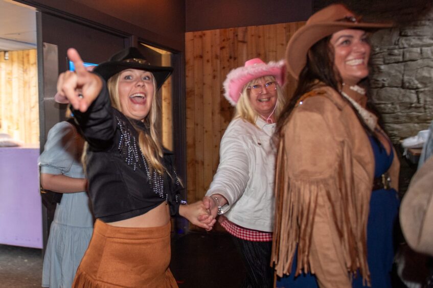 Women dressed in cowboy hats enter a nightclub. 
