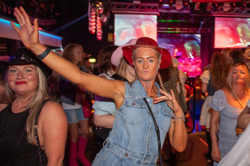 A woman in country-and-western garb on the dancefloor in a nightclub. 