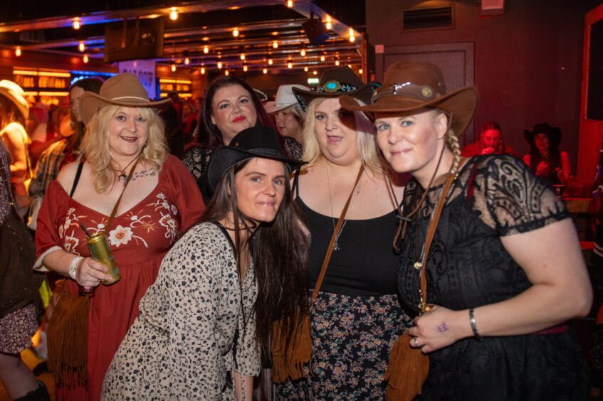 Five women, four of them in cowboy hats, pose in a nightclub. 