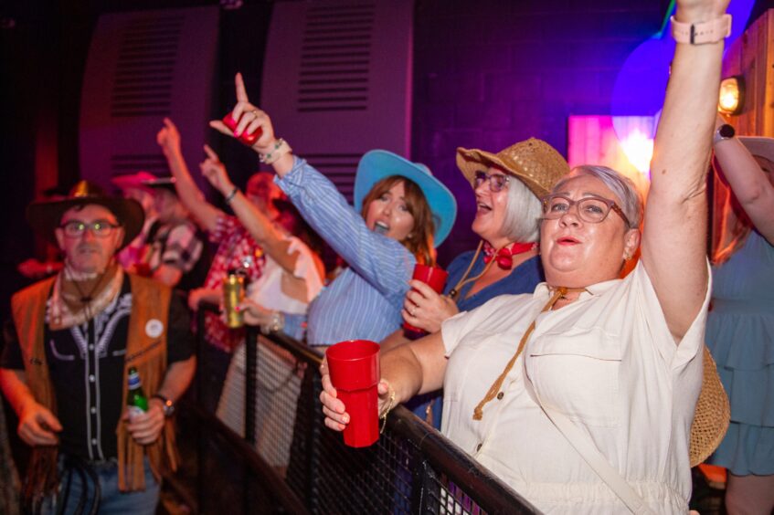 Revellers, many in cowboy hats, with their hands in the air at a nightclub. 