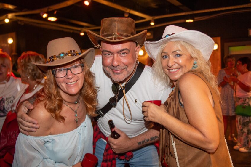A man and two women, all in cowboy hats, pose in a nightclub. 