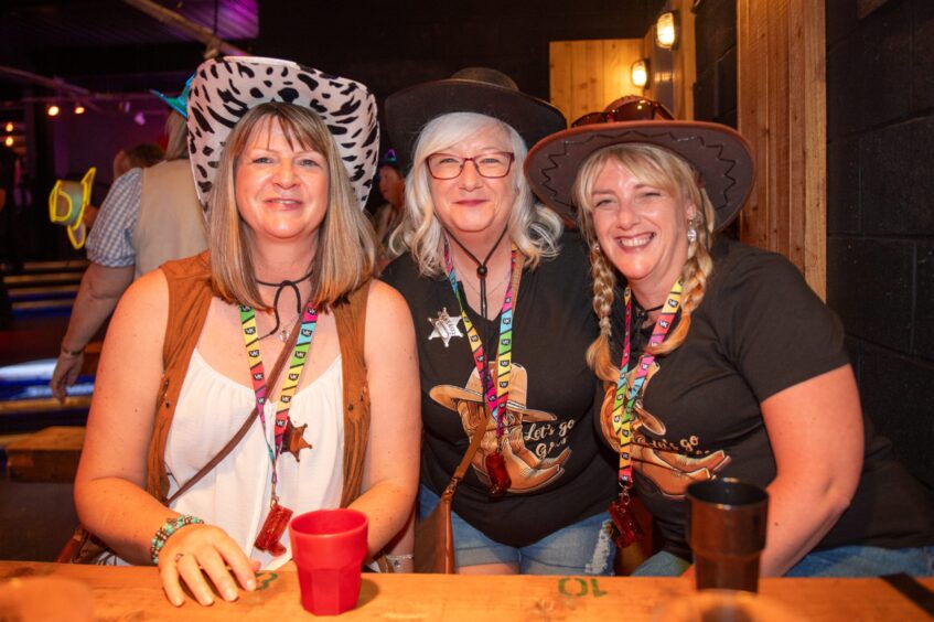 Three women wearing cowboy hats at a nightclub table. 